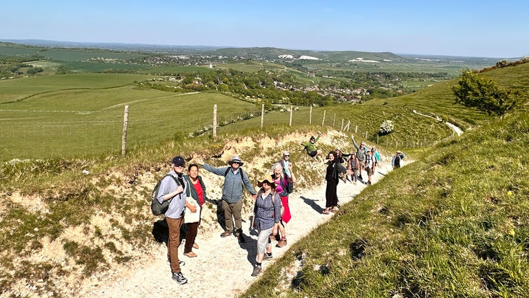 A group of people stand and wave from a sunny path on the South Downs